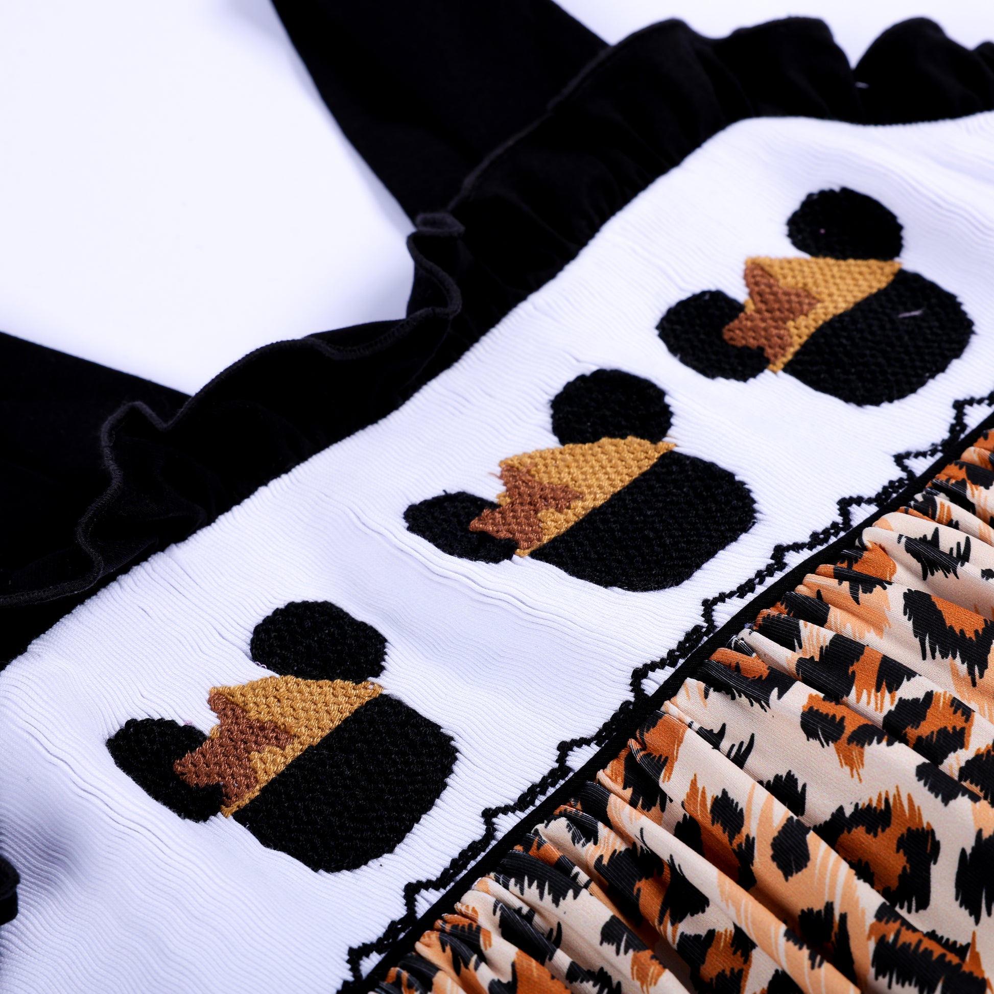 Detailed close up shot of hand embroidered safari mouse heads on white smocked chest panel of leopard dress.
