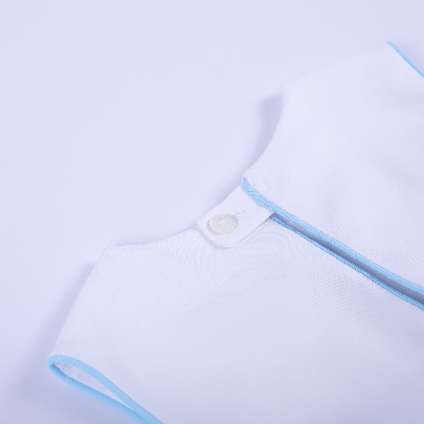 Close-up detail of back neck white button closure and blue trim piping on classic baby boy bubble outfit.