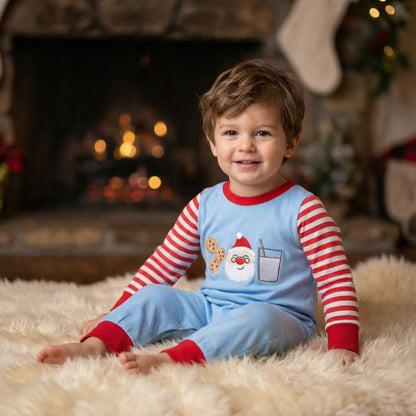 Baby boy sitting on rug by fireplace wearing blue milk and cookies Santa Christmas romper.