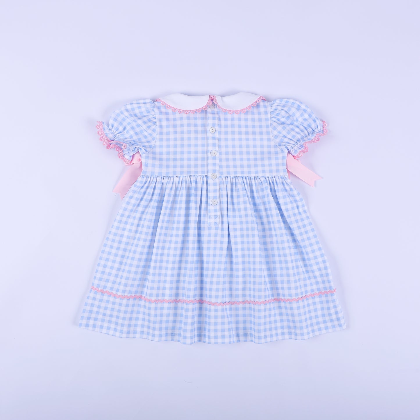 Full back view of light blue gingham gender reveal smocked dress showing white button closures and puffed sleeves.