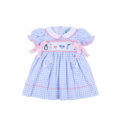 Front view of light blue gingham gender reveal smocked dress with pink bows and hand embroidered baby stork details.
