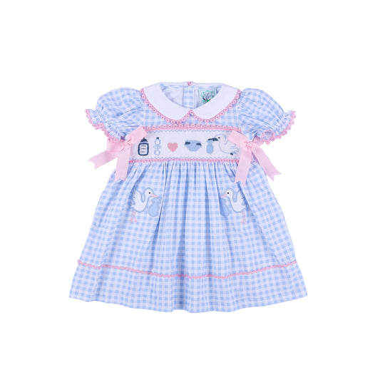 Front view of light blue gingham gender reveal smocked dress with pink bows and hand embroidered baby stork details.