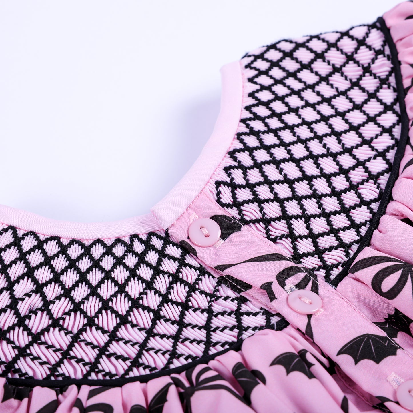 Close-up of pink button closure and hand smocked lattice neck detailing on back of Halloween baby top.