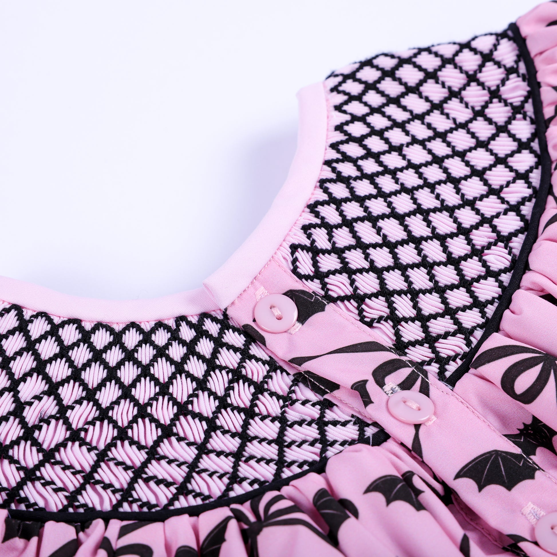 Close-up of pink button closure and hand smocked lattice neck detailing on back of Halloween baby top.