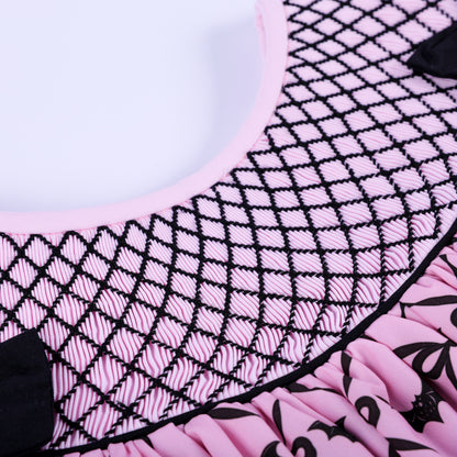 Macro close-up of intricate hand smocked black lattice embroidery stitching on pink Halloween dress collar.