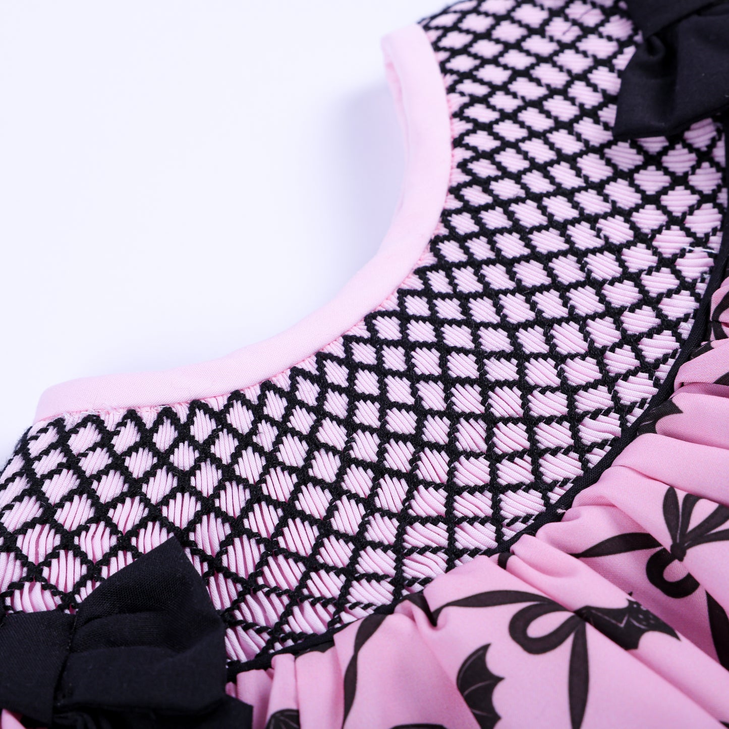Detailed view of intricate black hand embroidered lattice smocking stitches on pink Halloween baby top.