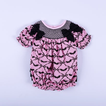 Pink Halloween baby girl hand smocked bubble outfit featuring black bat print and bow accent details.