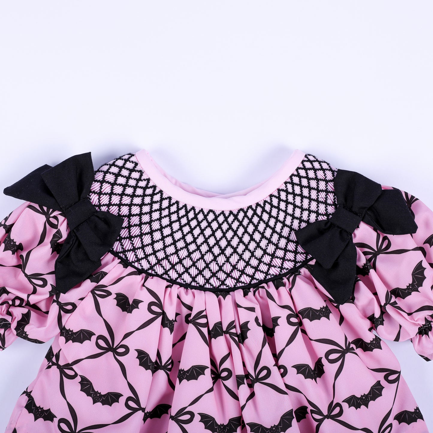 Hand smocked black lattice neckline detail on a pink bat pattern baby girl top with black side bows.