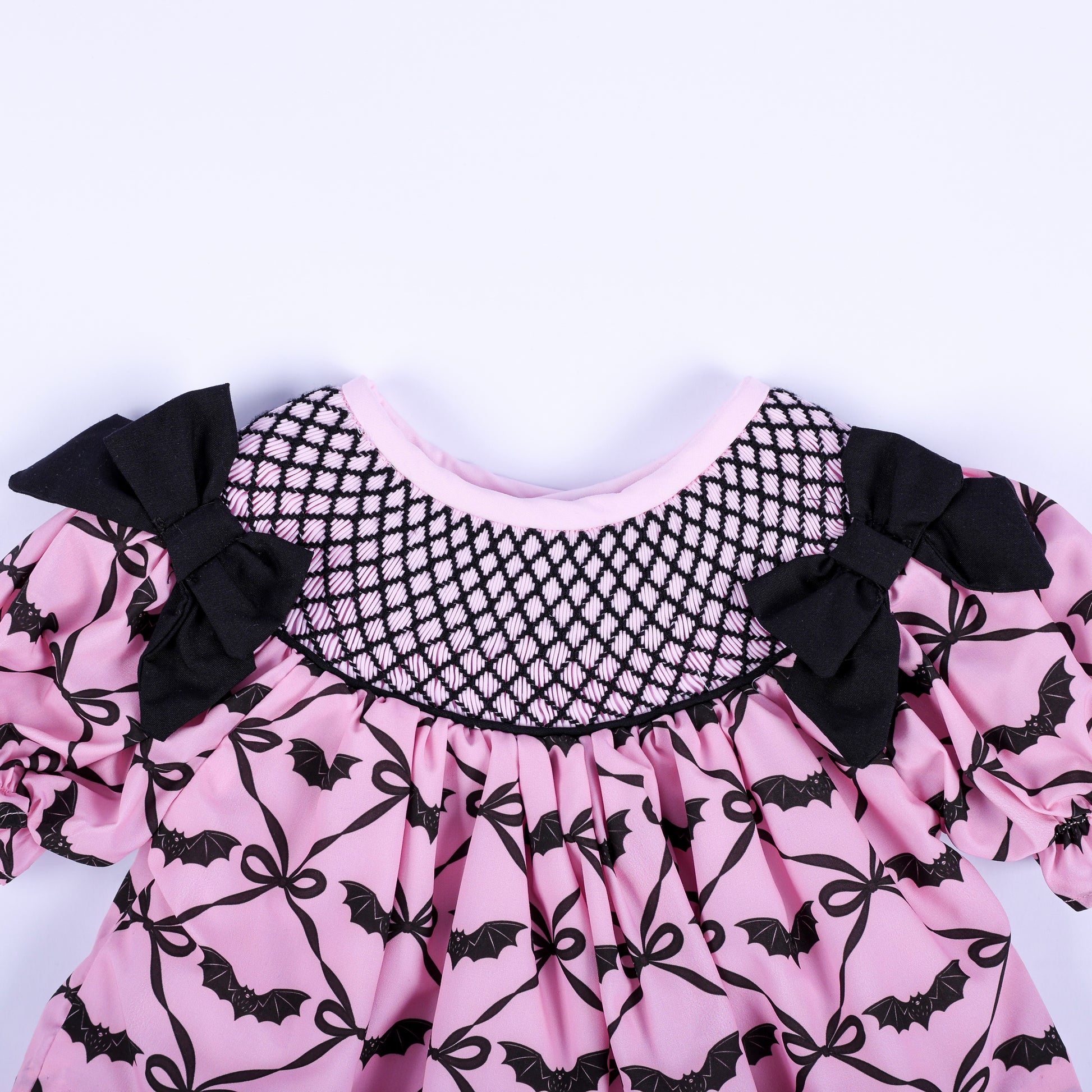 Hand smocked black lattice neckline detail on a pink bat pattern baby girl top with black side bows.