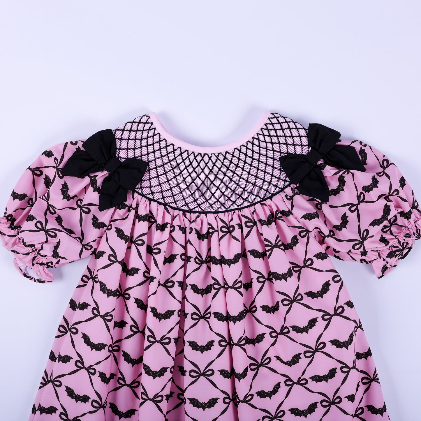 Front bodice detail of girls pink hand smocked dress with black lattice yoke stitching and shoulder bows.
