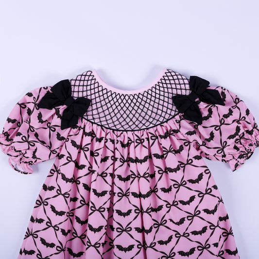 Front bodice detail of girls pink hand smocked dress with black lattice yoke stitching and shoulder bows.