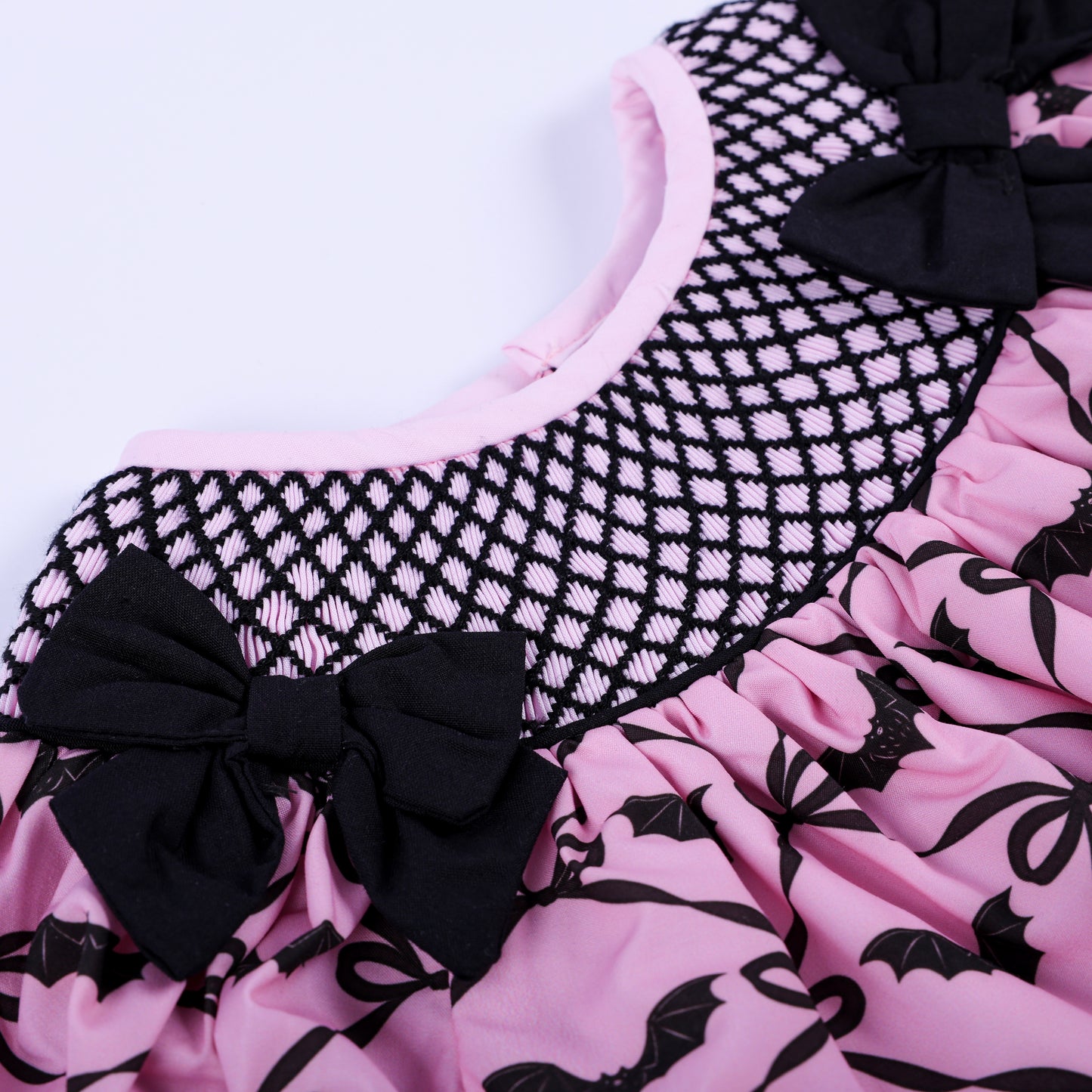 Intricate black hand-smocked lattice stitching on pink Halloween baby girl outfit with black shoulder bows.