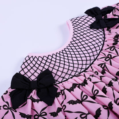Angled view highlighting hand smocked geometric black yoke and shoulder bow on pink bat bow toddler dress.