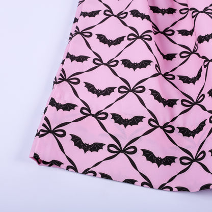 Close-up of pink dress fabric showing black bats inside ribbon bow lattice grid pattern on skirt hem.