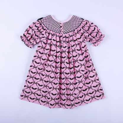 Full back view of pink hand smocked dress showing rear button placket closure and black bat bow pattern.