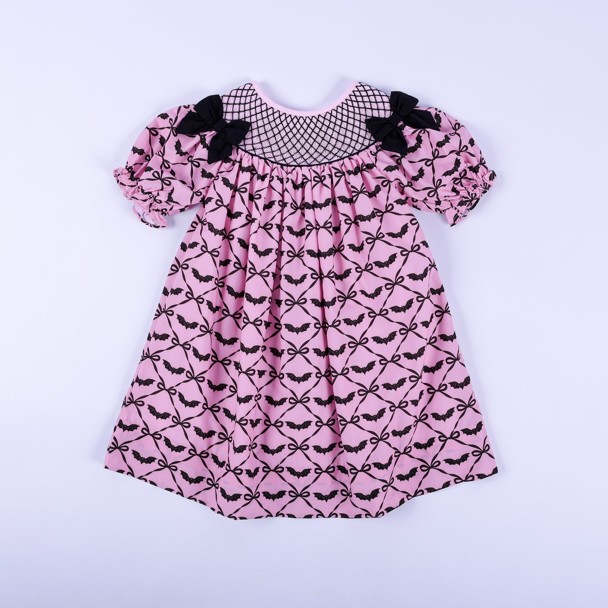 Pink hand smocked Halloween dress for girls featuring black bat bow print, black yoke embroidery, and puff sleeves.