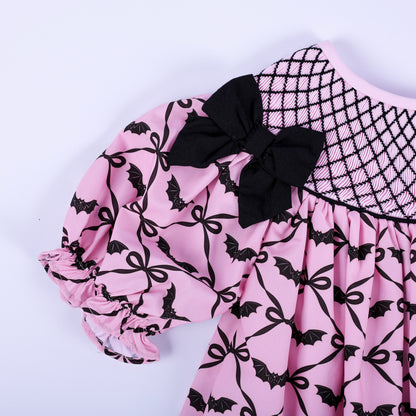 Detail view of puff sleeve with ruffle cuff and black accent bow on pink bat print hand smocked dress.