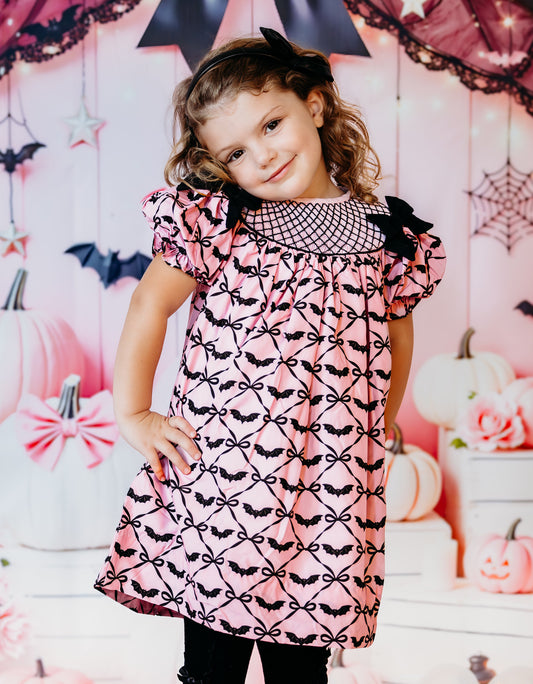 Girl posing in the Batty for Bows hand smocked pink Halloween dress with black hand embroidered bat print.