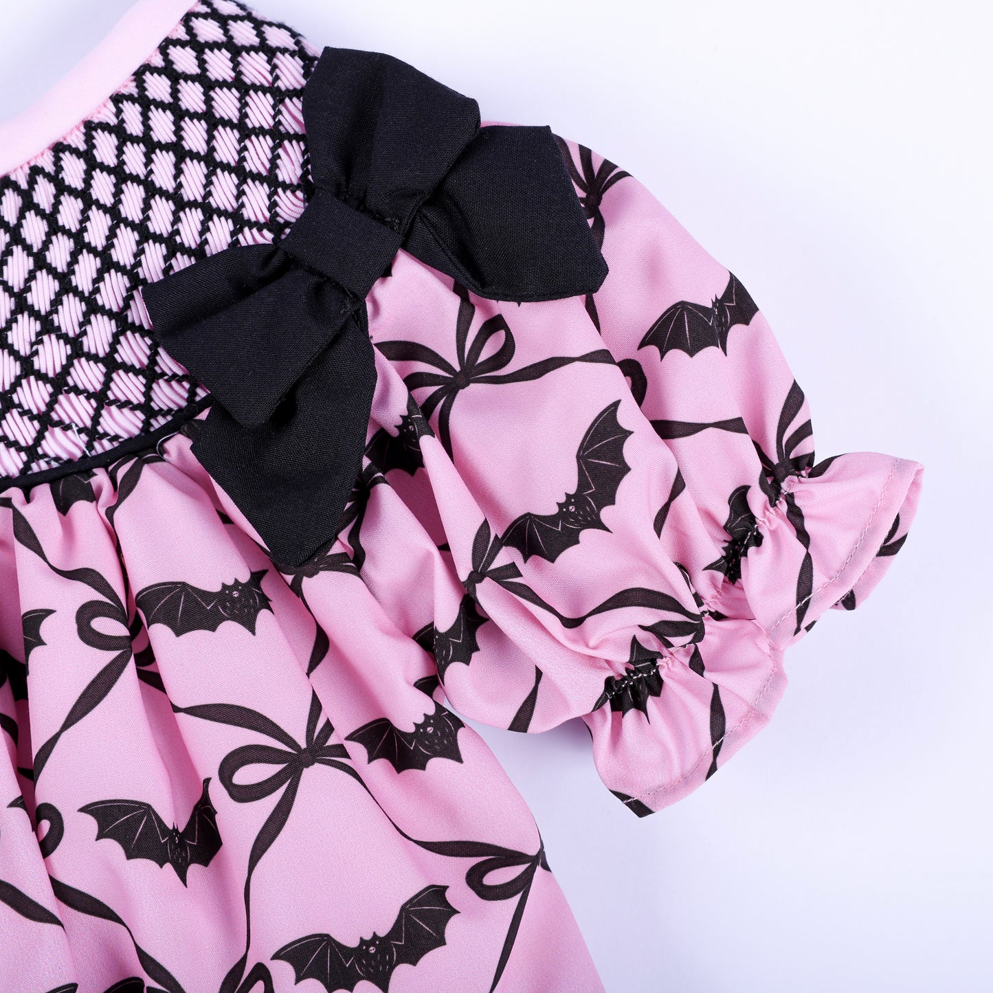 Close-up of puffed short sleeve with ruffle trim and black fabric bow on pink bat print smocked top.
