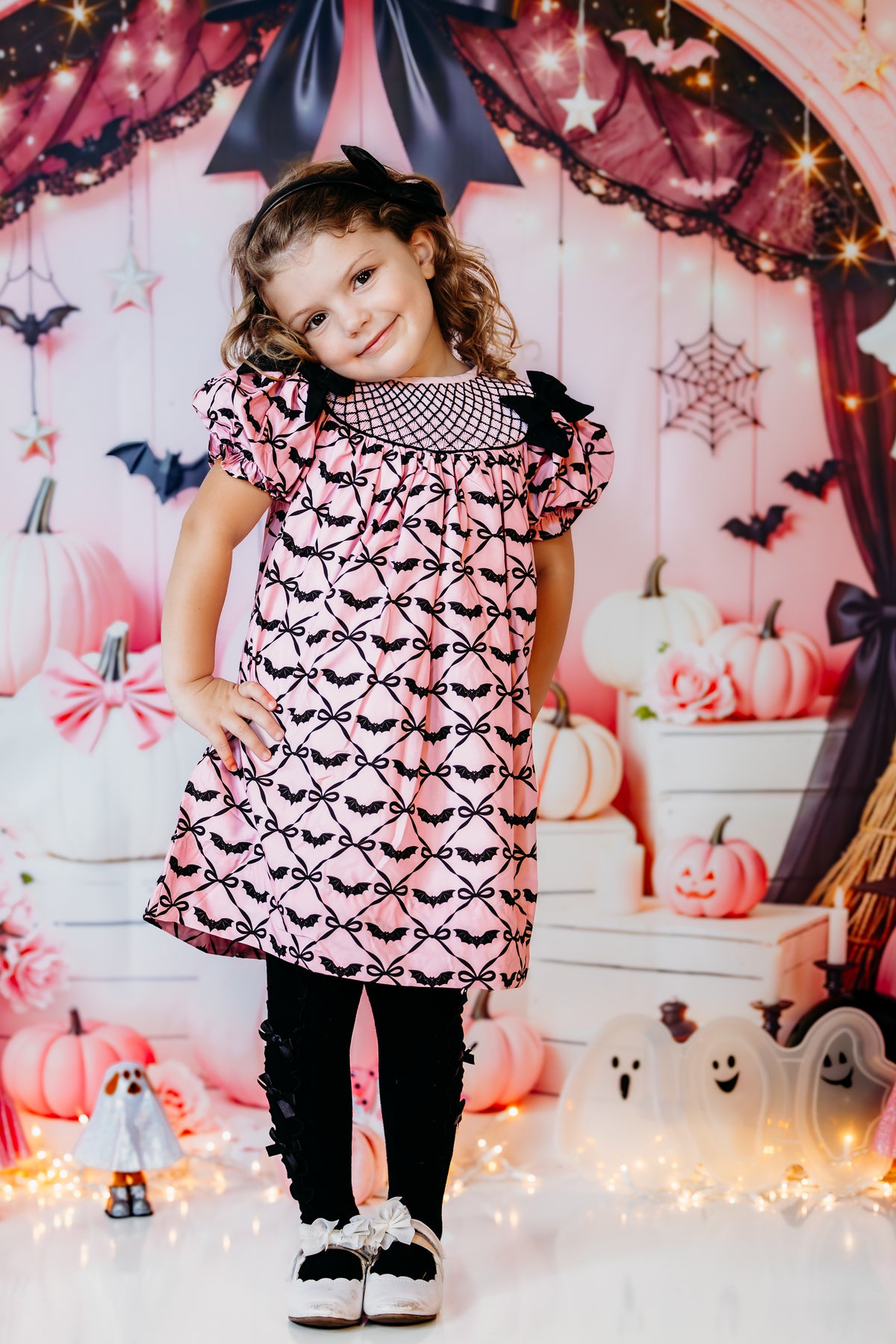 Full-length view of toddler girl wearing the Batty for Bows hand smocked Halloween dress with black bat bows.