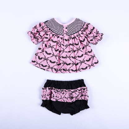 Full back view of pink bat print smocked top with button closure and matching black ruffled bloomers.