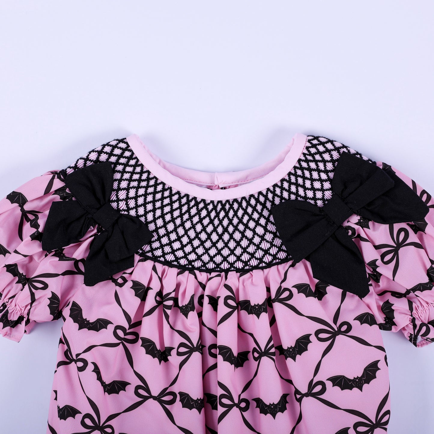 Close-up of pink Halloween baby bubble with black hand-smocked neck yoke and decorative fabric bow accents.