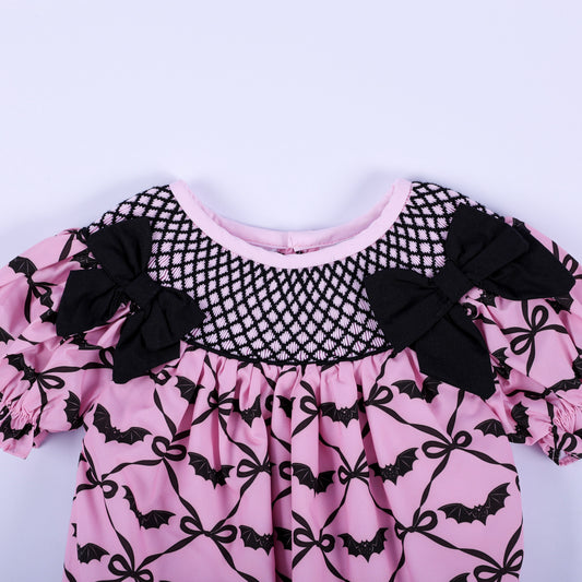 Close-up of pink Halloween baby bubble with black hand-smocked neck yoke and decorative fabric bow accents.