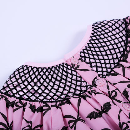 Close-up of pink button closure on back of hand-smocked pink and black bat print baby Halloween bubble.