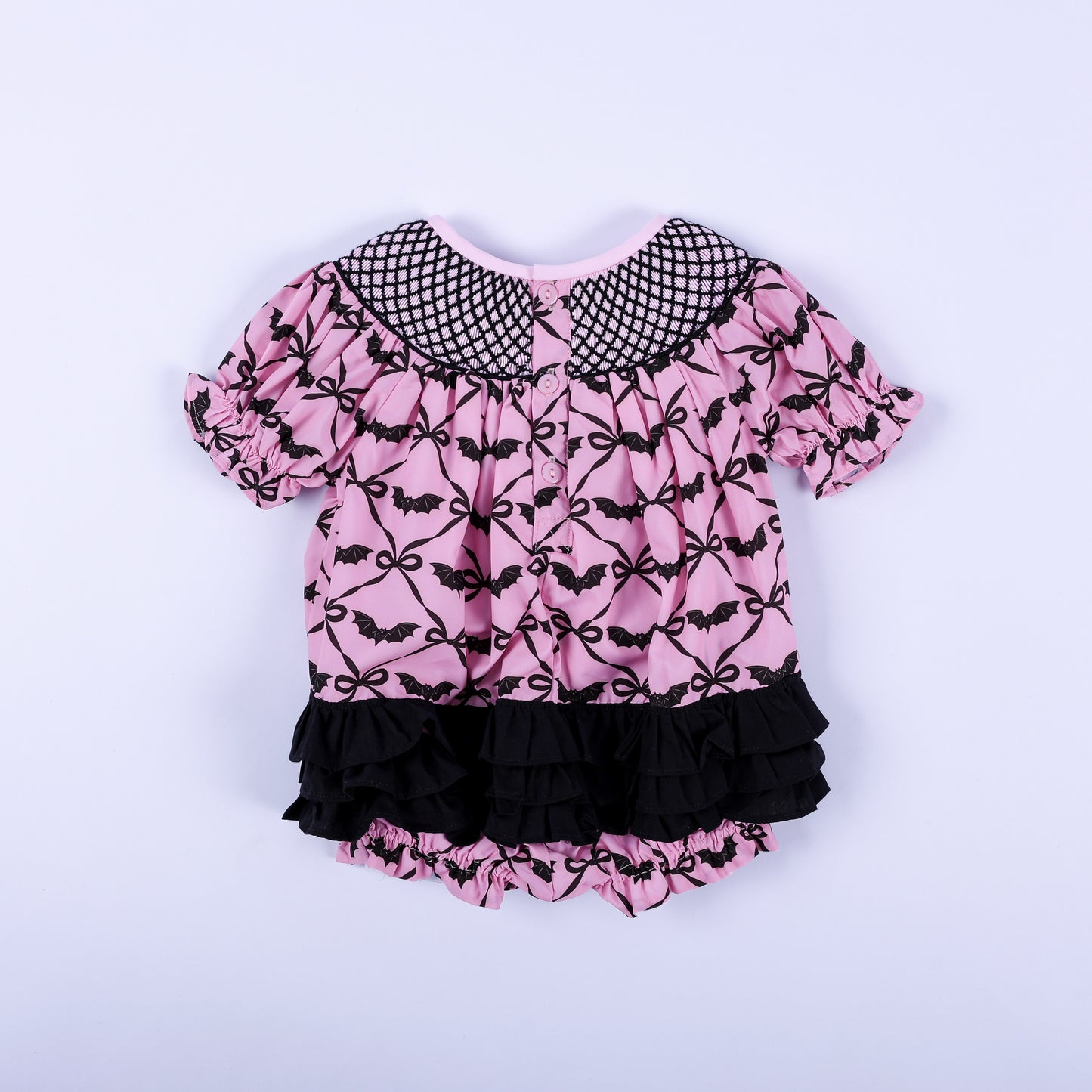 Back view of pink Halloween baby smocked bubble featuring tiered black ruffles and back button closure.