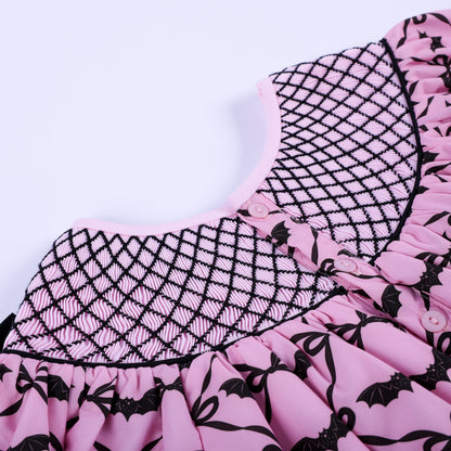 Close-up back view of hand smocked neck yoke showing pink button closures and black embroidery detail.