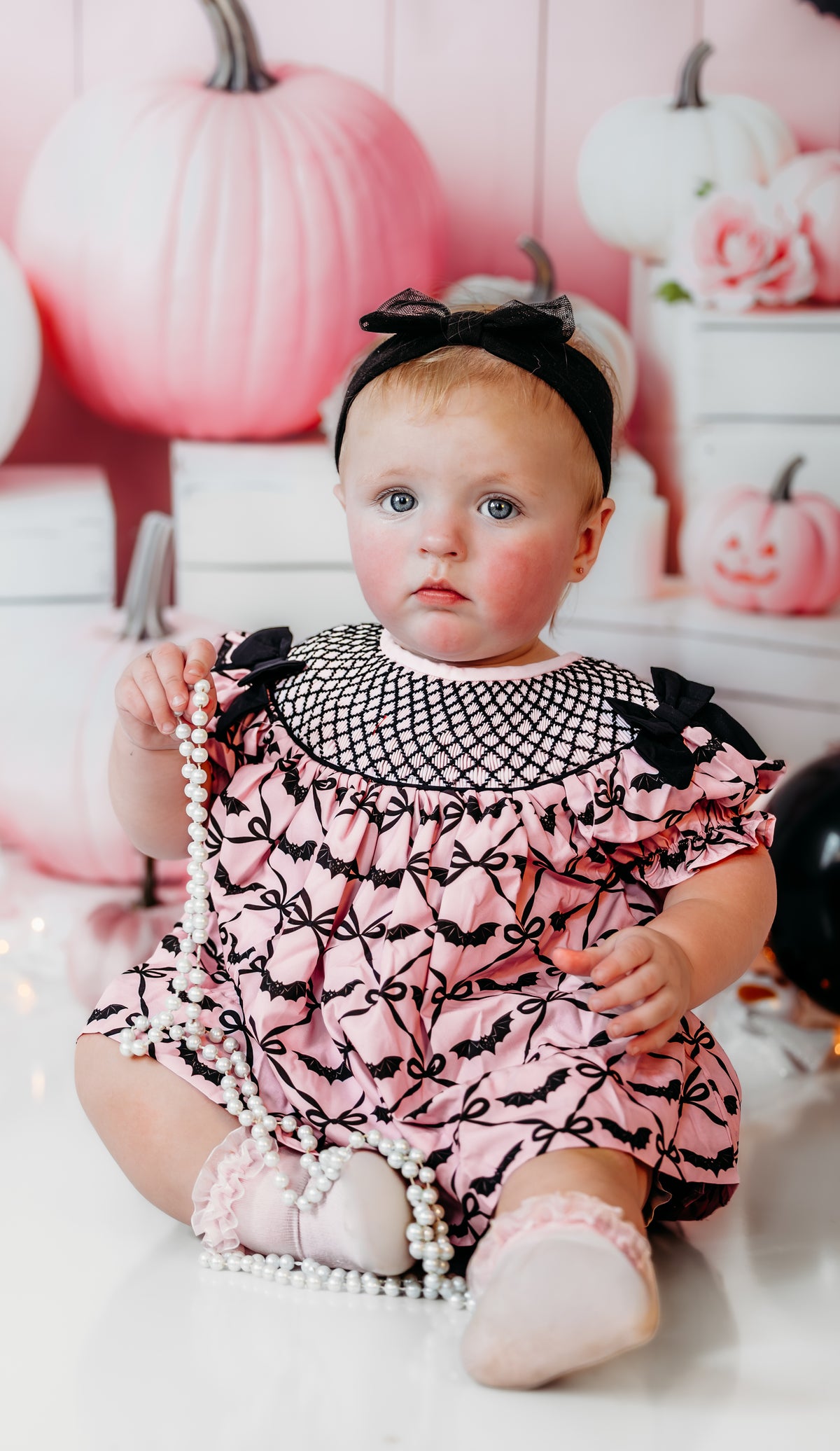 Front view of baby girl sitting in Batty for Bows hand smocked embroidered bats bloomer set with bow headband.