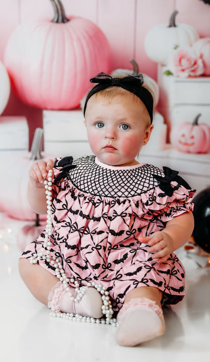 Front view of baby girl sitting in Batty for Bows hand smocked embroidered bats bloomer set with bow headband.