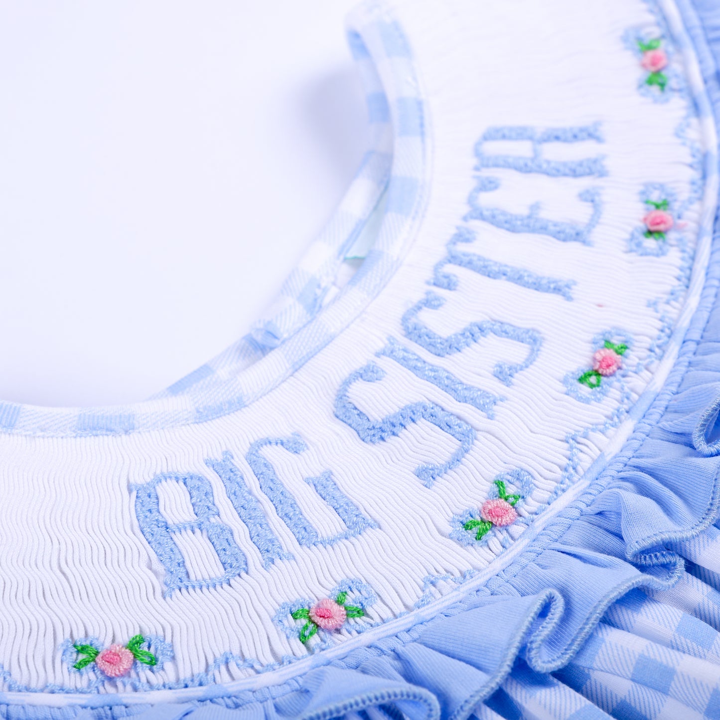 Detailed view of hand-smocked Big Sister embroidered lettering and embroidered flowers on white collar.