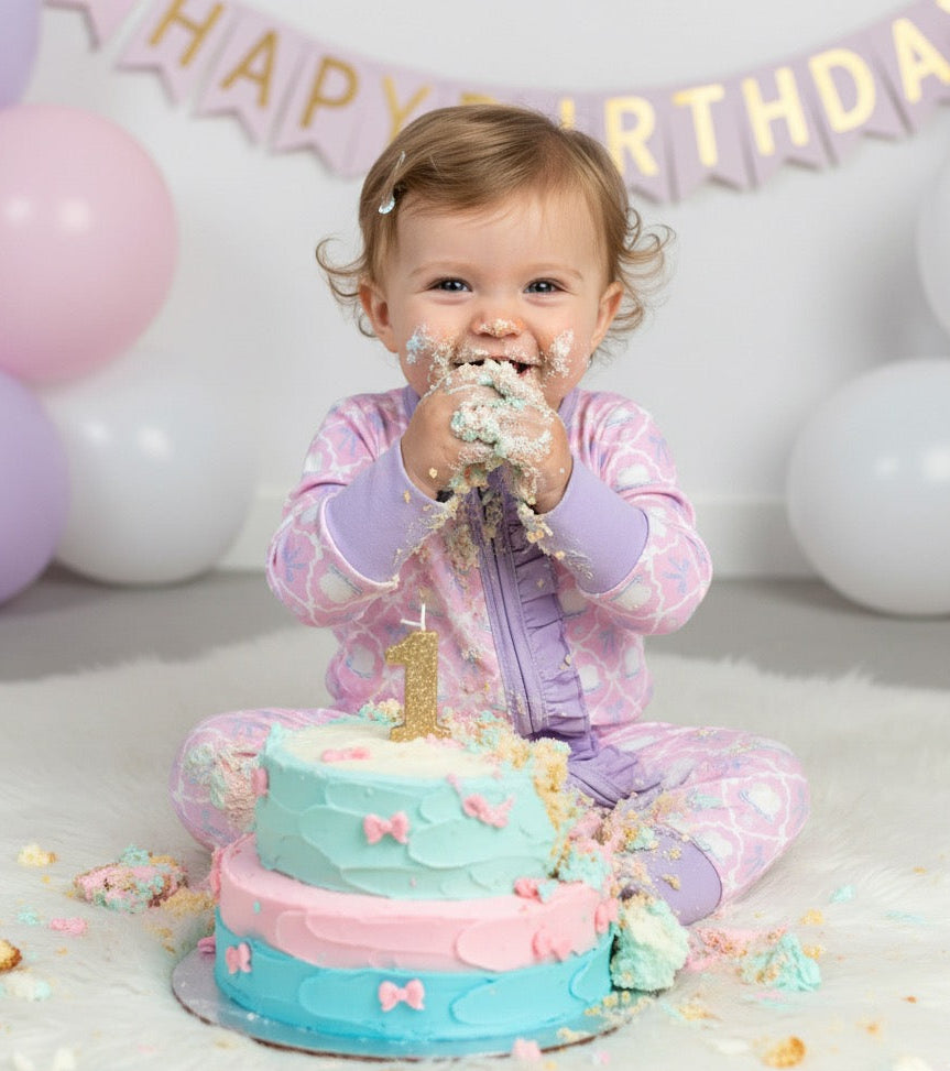 Baby girl wearing the Birthday Cake and Bow Girl Zippy enjoying a 1st birthday cake smash photo session.