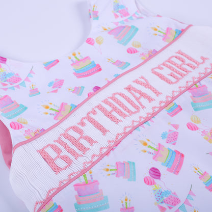 Angled texture shot of the pink hand embroidered birthday girl lettering on white smocked fabric baby girl top.