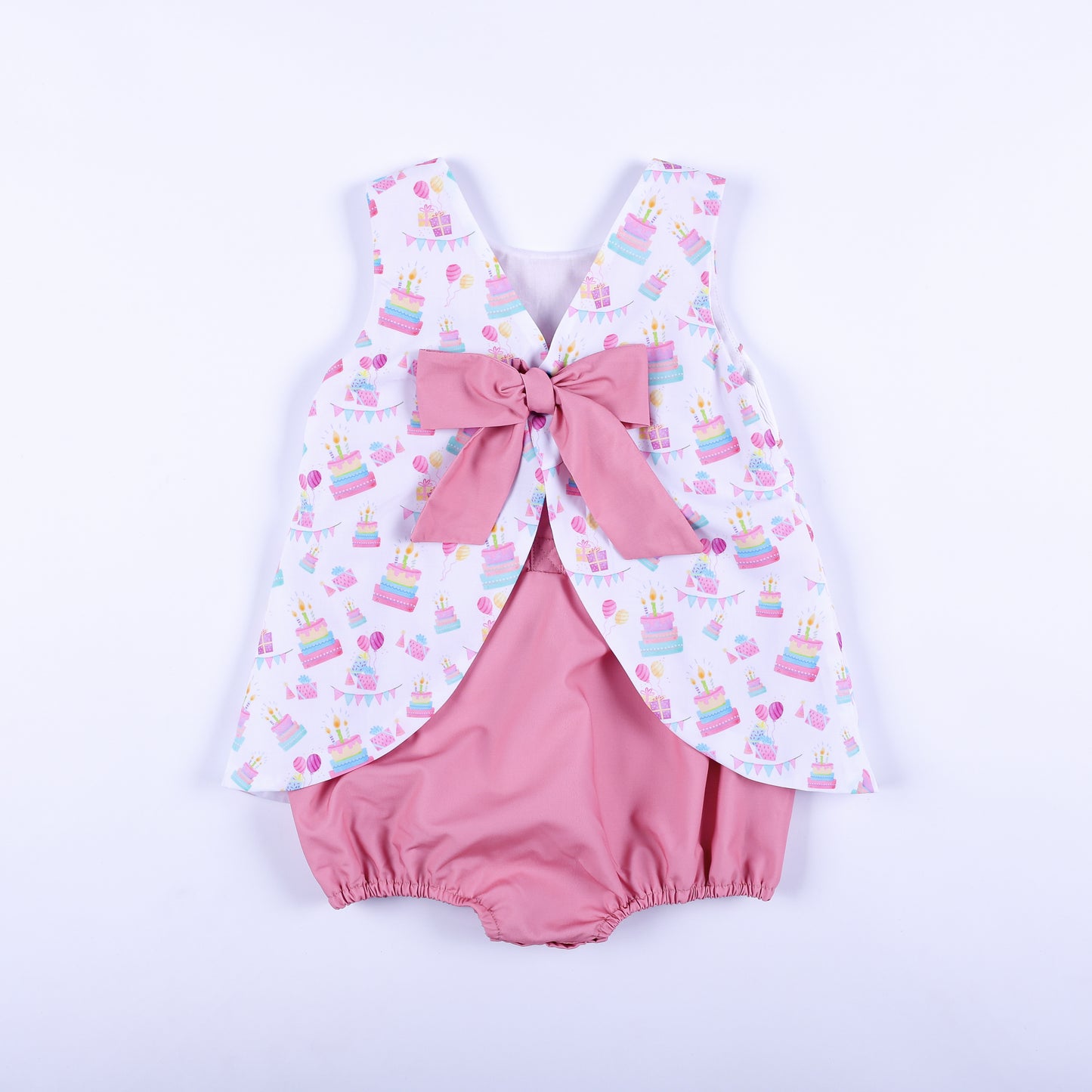 Back view of a birthday girl hand smocked bubble outfit featuring a large pink bow tie over bloomers.