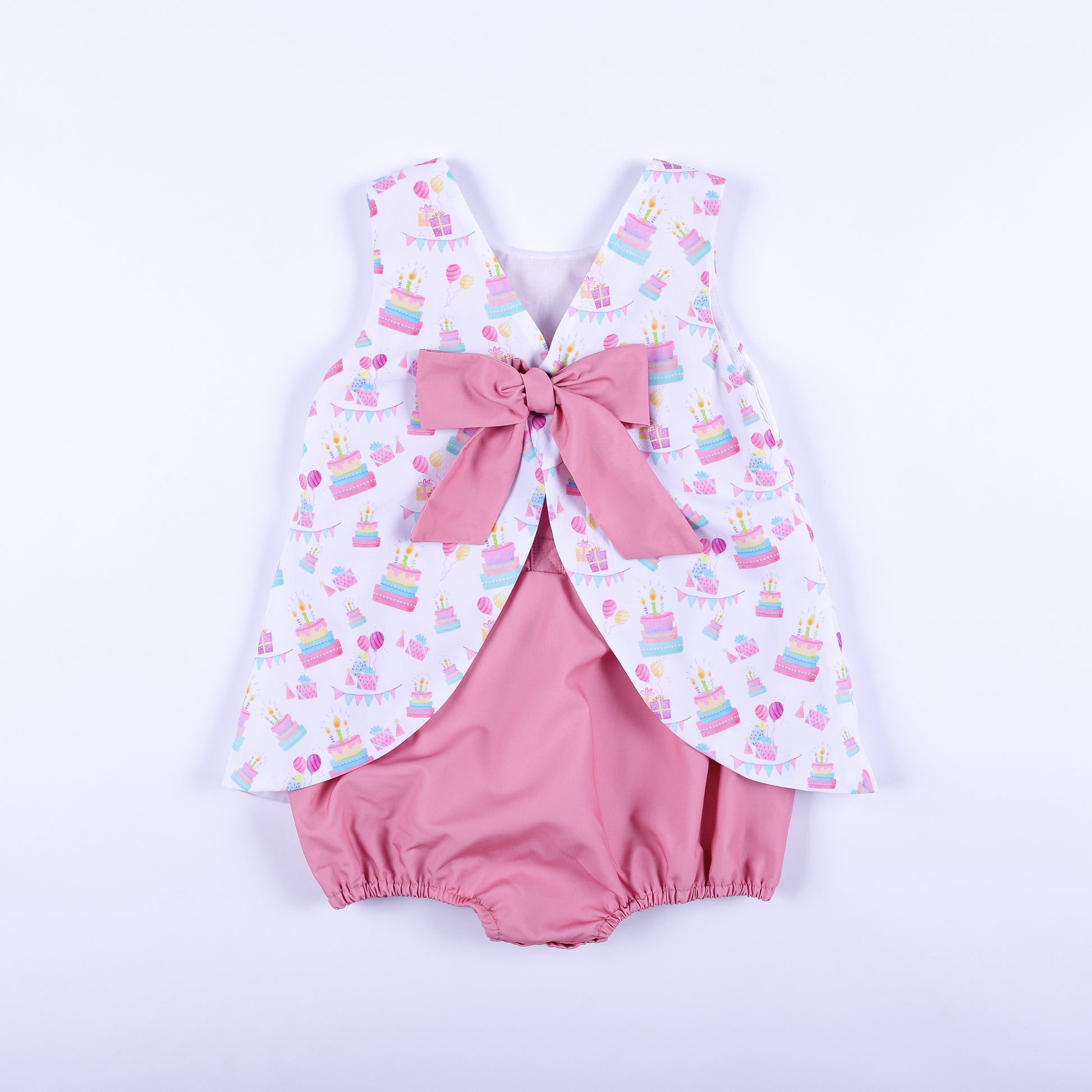 Back view of a birthday girl hand smocked bubble outfit featuring a large pink bow tie over bloomers.