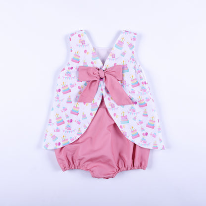 Back view of a birthday girl hand smocked bubble outfit featuring a large pink bow tie over bloomers.