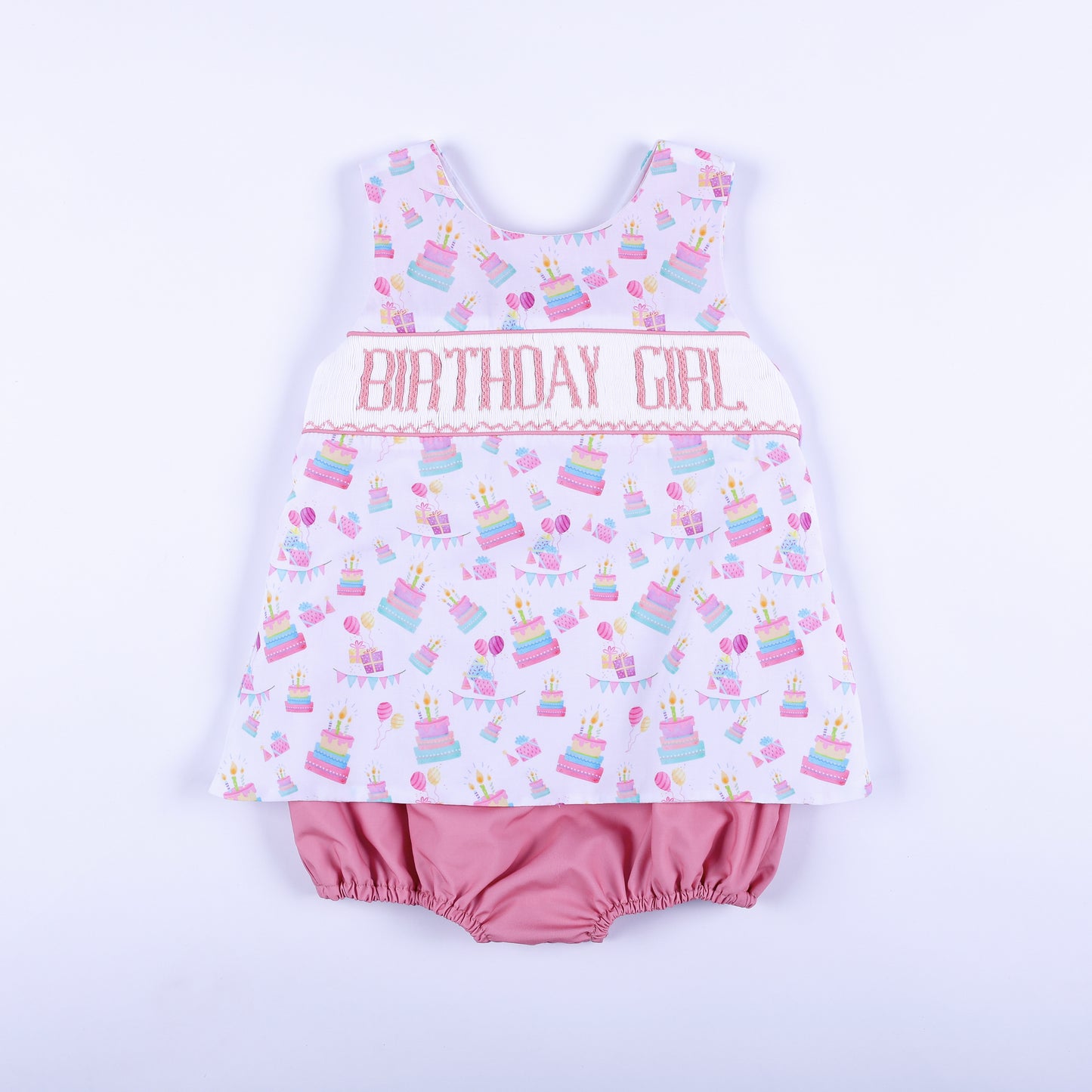 Front view of a pink birthday girl hand smocked bubble outfit with hand embroidery and cake print.