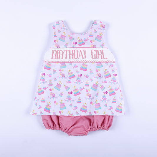 Front view of a pink birthday girl hand smocked bubble outfit with hand embroidery and cake print.