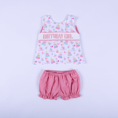 Front view of birthday girl hand smocked bloomer set featuring a pastel cake print swing top and pink ruffle shorts.