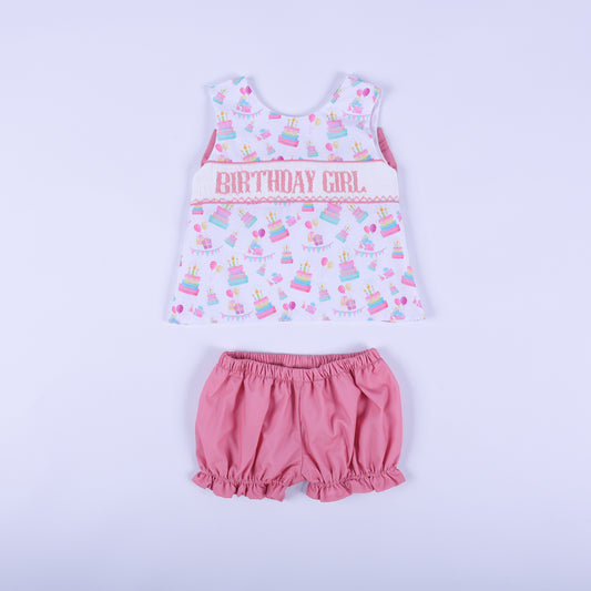 Front view of birthday girl hand smocked bloomer set featuring a pastel cake print swing top and pink ruffle shorts.