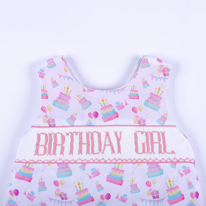 Close-up of hand smocked bodice with pink Birthday Girl hand embroidery on a white cake print background.