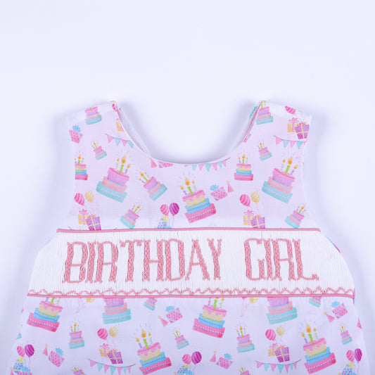 Close-up of hand smocked bodice with pink Birthday Girl hand embroidery on a white cake print background.