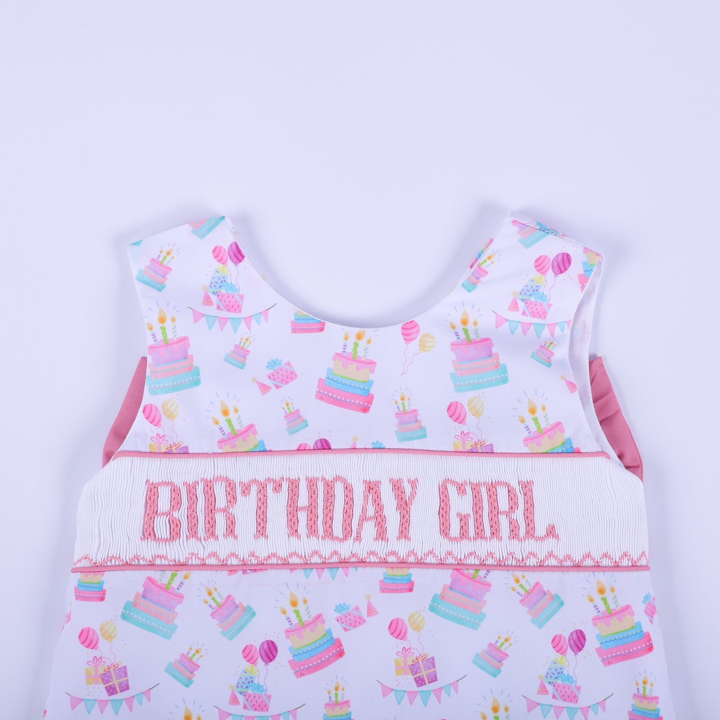 Close-up of the birthday girl hand smocked top bodice showing pink embroidered lettering and pastel birthday cakes.
