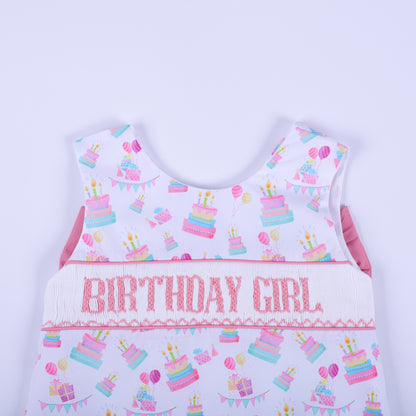 Close-up of the birthday girl hand smocked top bodice showing pink embroidered lettering and pastel birthday cakes.