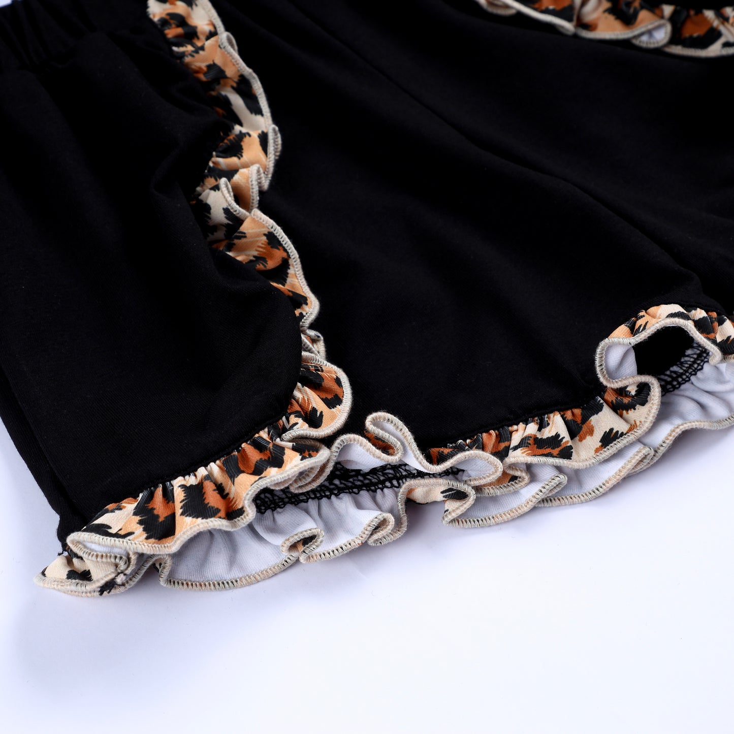 Detailed view of the leopard print ruffle trim along the hemline of black toddler girls boutique shorts.
