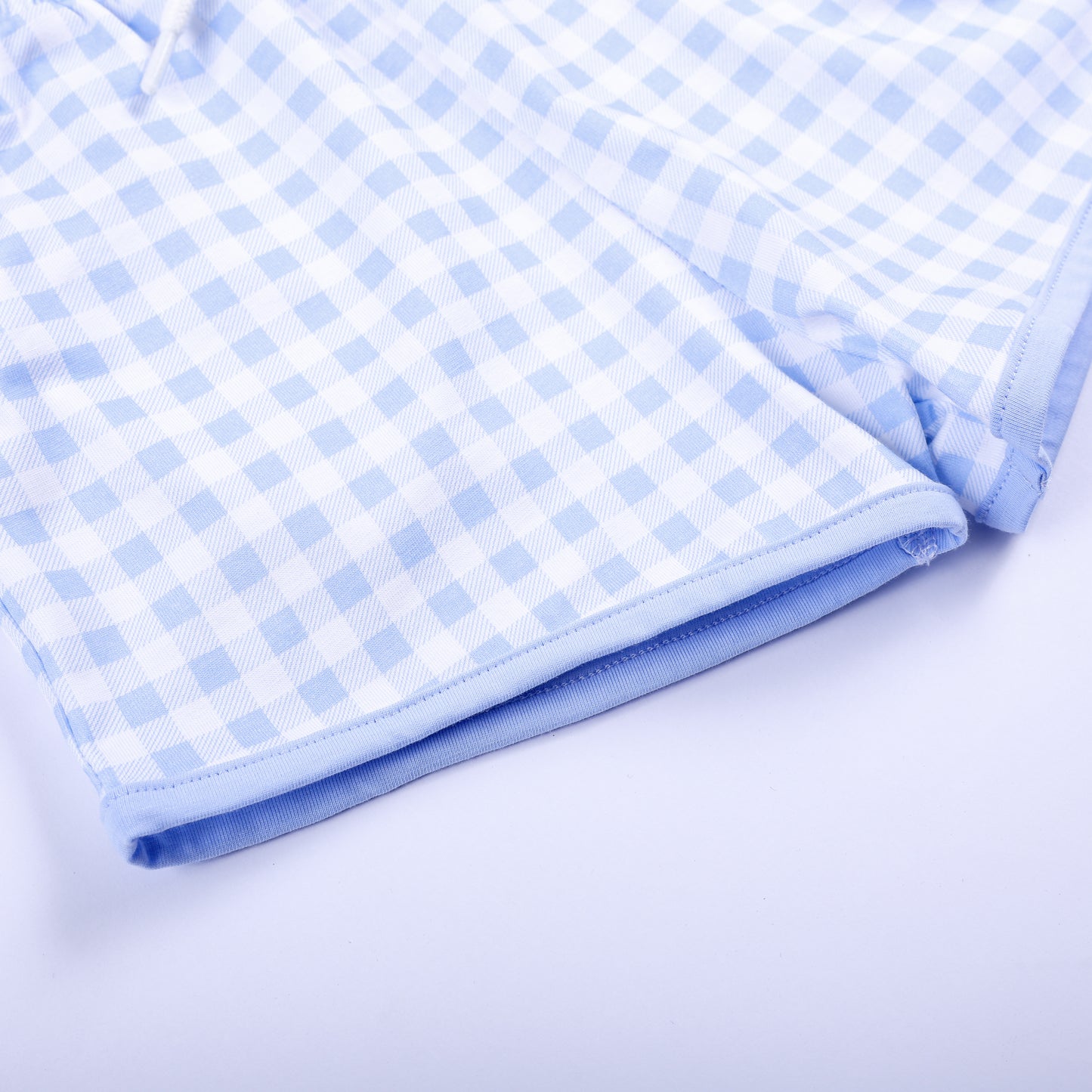 Close-up shot of neat hem stitching on light blue gingham shorts matching hand smocked Big Brother outfit.