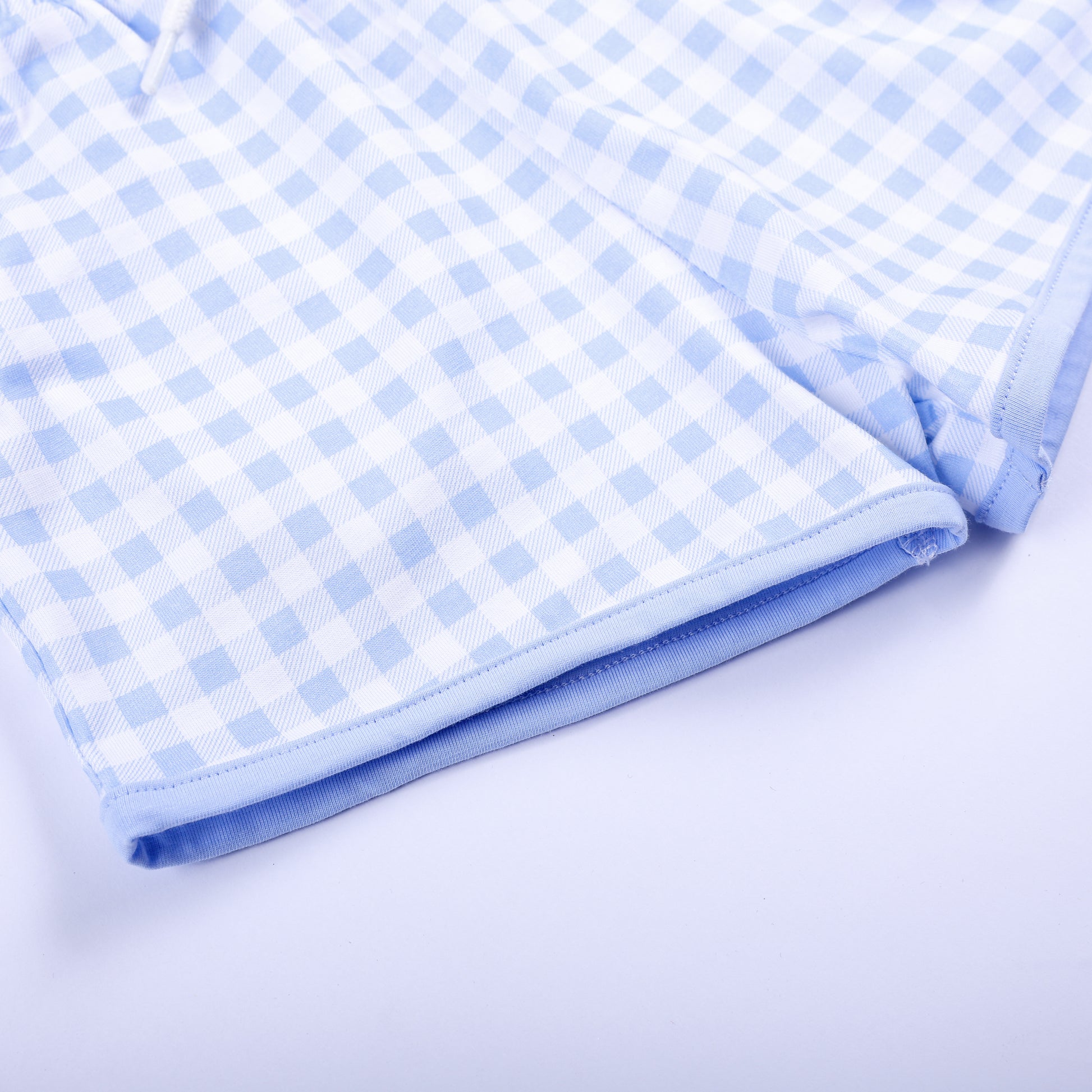 Close-up shot of neat hem stitching on light blue gingham shorts matching hand smocked Big Brother outfit.