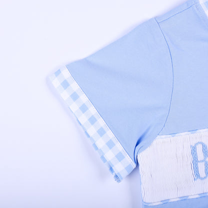 Detailed view of short sleeve with blue gingham plaid trim on light blue hand smocked Big Brother kids shirt.